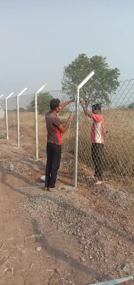 Two workers fixing chain-link mesh to galvanised fence posts